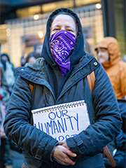 A woman at a Democracy Rising protest against ICE clutches a sign that reads 'Our Humanity', and her clutched hands cover up the rest of the message. 